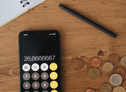 Image of calculator app on phone along with changes lying around and financial paper.